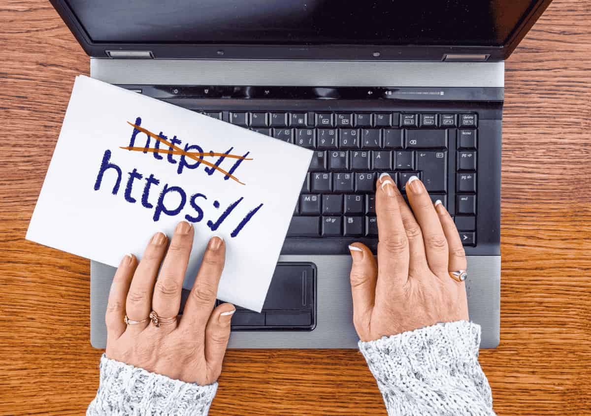 Hands typing on a laptop beside note showing http crossed out and https written below Hands typing on a laptop beside note showing http crossed out and https written below