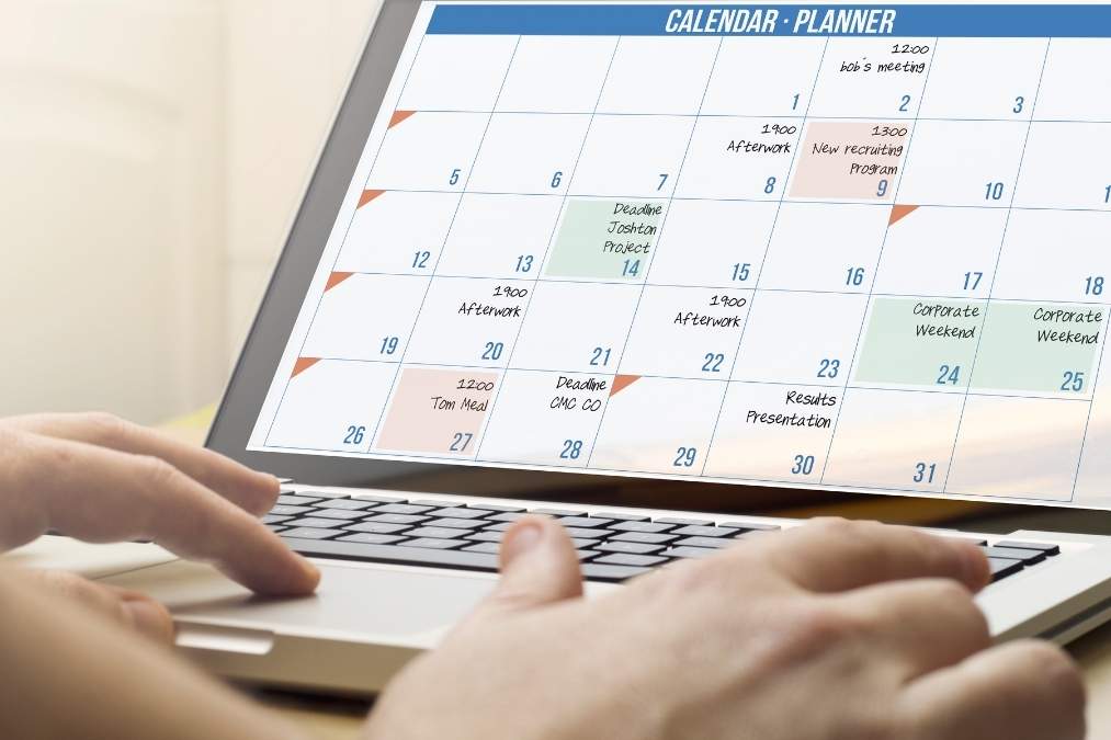 Close-up of a laptop screen displaying a monthly calendar planner with various scheduled meetings and deadlines.