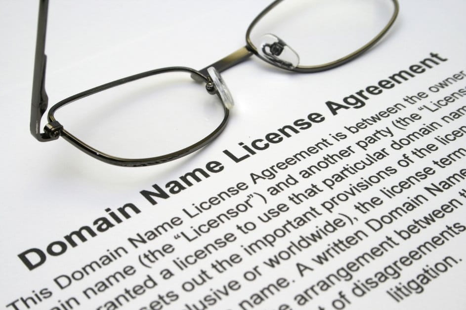 Close-up of a "Domain Name License Agreement" document with a pair of eyeglasses resting on the page.